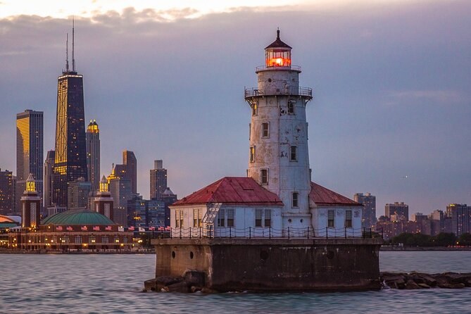 The harbor lighthouse at dusk, its lamp lit, the towers beyond
