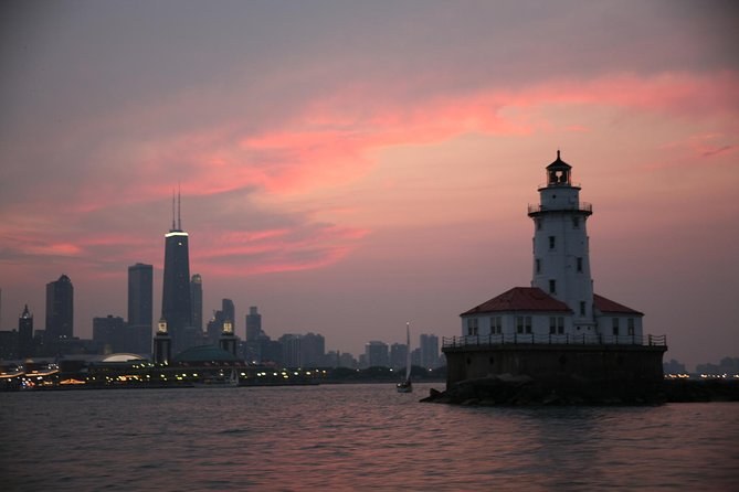 A harbor lighthouse on the lake with the skyline behind it under a pink sky