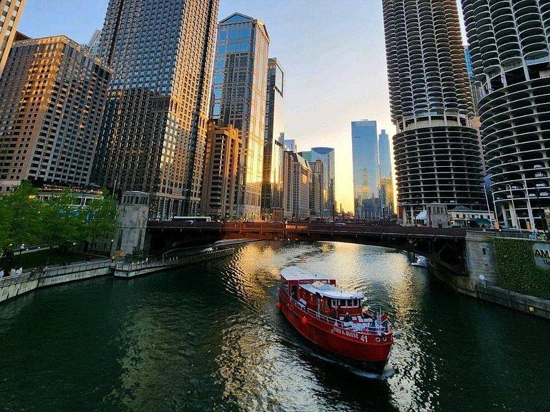 A small boat on the river between tall towers and a bridge