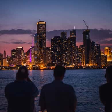 Two people on deck watching the skyline lights come on across the water